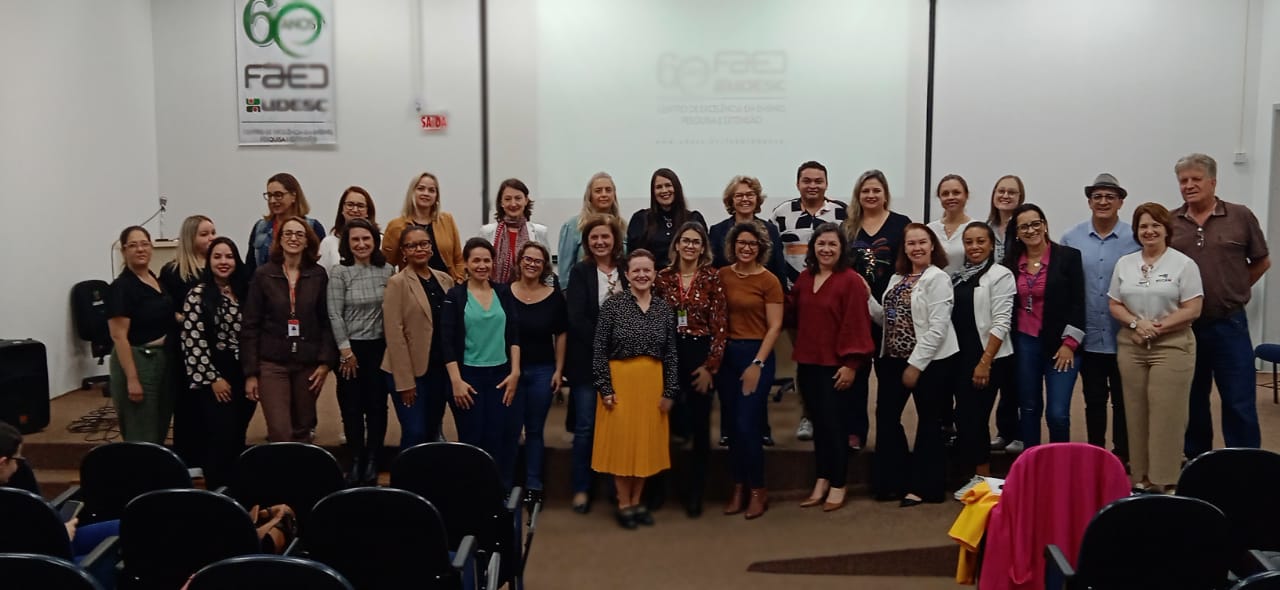 Cerca de 30 pessoas posam para foto em pé em auditório. 