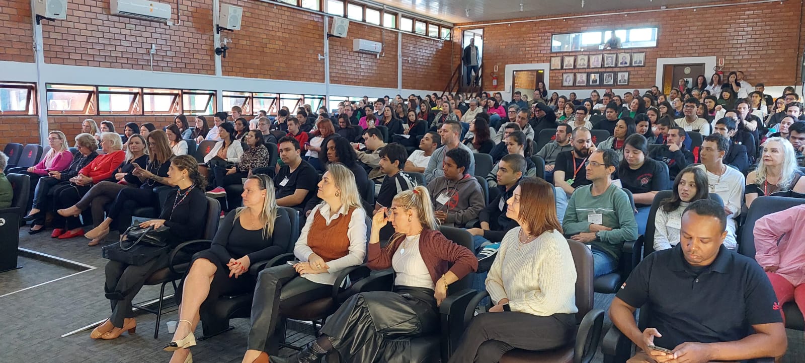 auditório lotado de pessoas sentadas assistindo a abertura do fórum