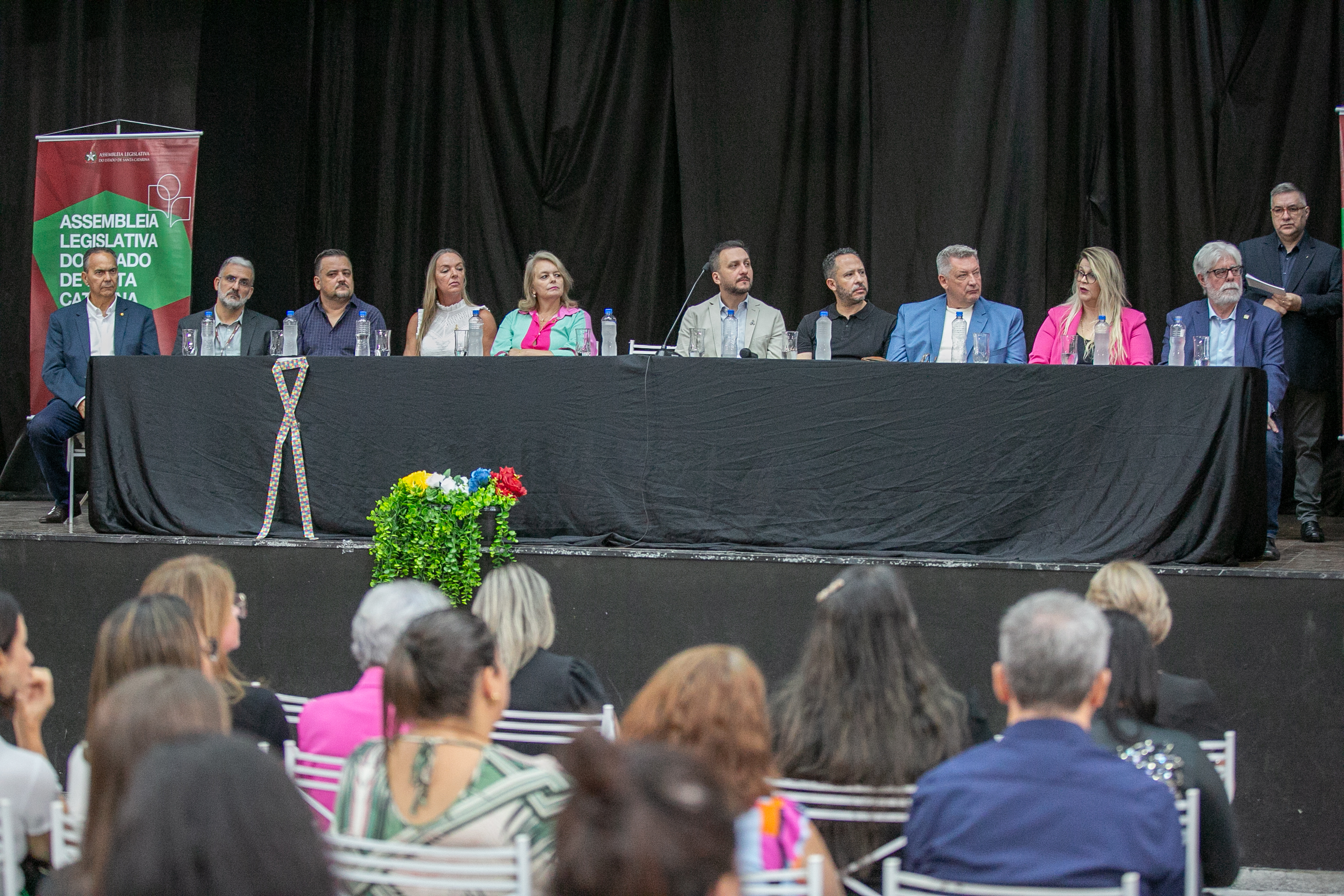 palco com mesa de autoridades, oito pessoas sentadas