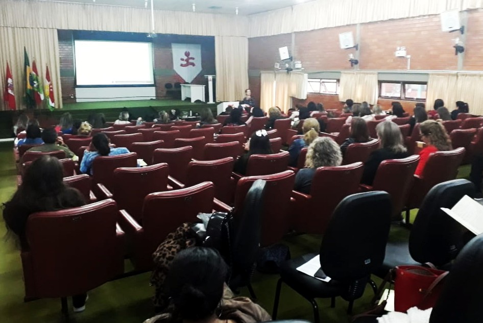 Imagem do auditório da FCEE lotado com professora em frente ao palco