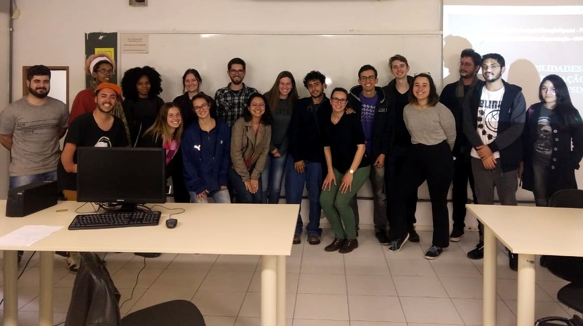 Turma de alunos com professora da FCEE no meio posam para foto em sala de aula.