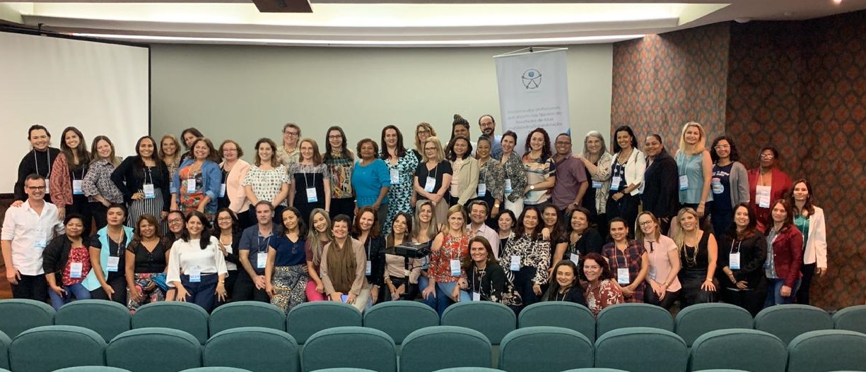 Grupo com dezenas de pessoas posa para foto em palco de auditório