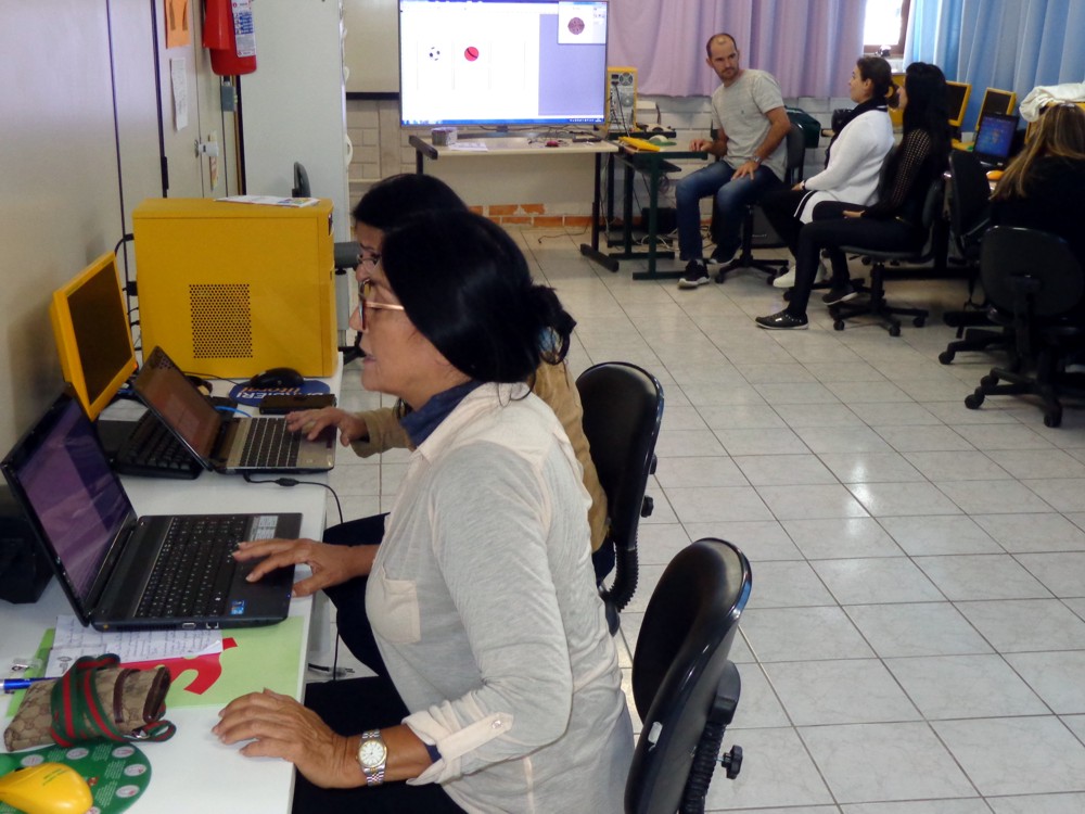 Professores diante de computadores acompanham o curso com professor ao fundo