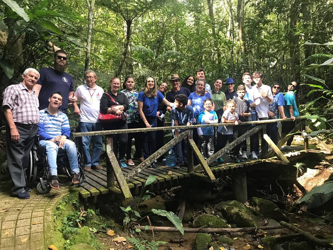 Grupo de cerca de 10 pessoas posam para foto em ponte de madeira sobre riacho em meio a mata fechada