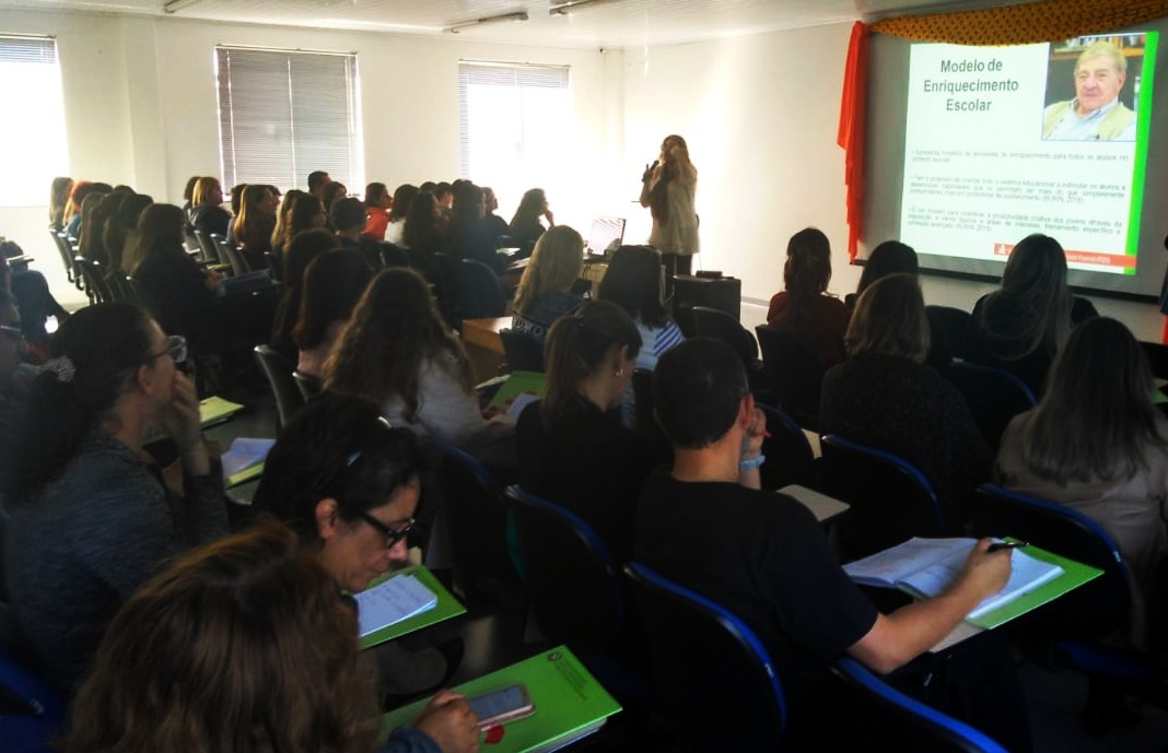 Sala de aula lotada, ao fundo telão com slide 