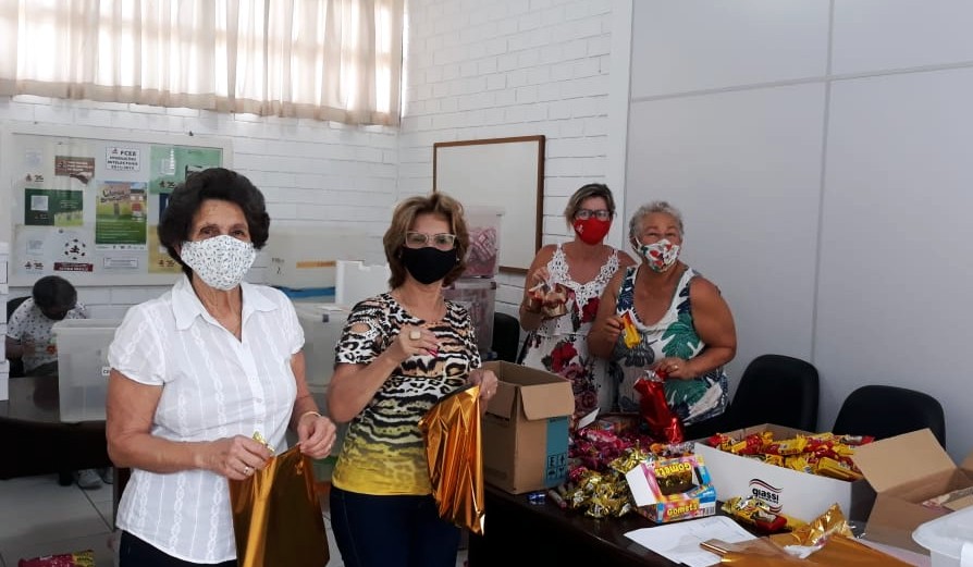 Quatro senhoras de máscaras posando para foto em meio a caixas com chocolates