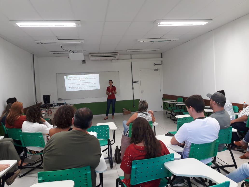 Psicóloga do Naahs em pé diante de professores sentados em sala de aula