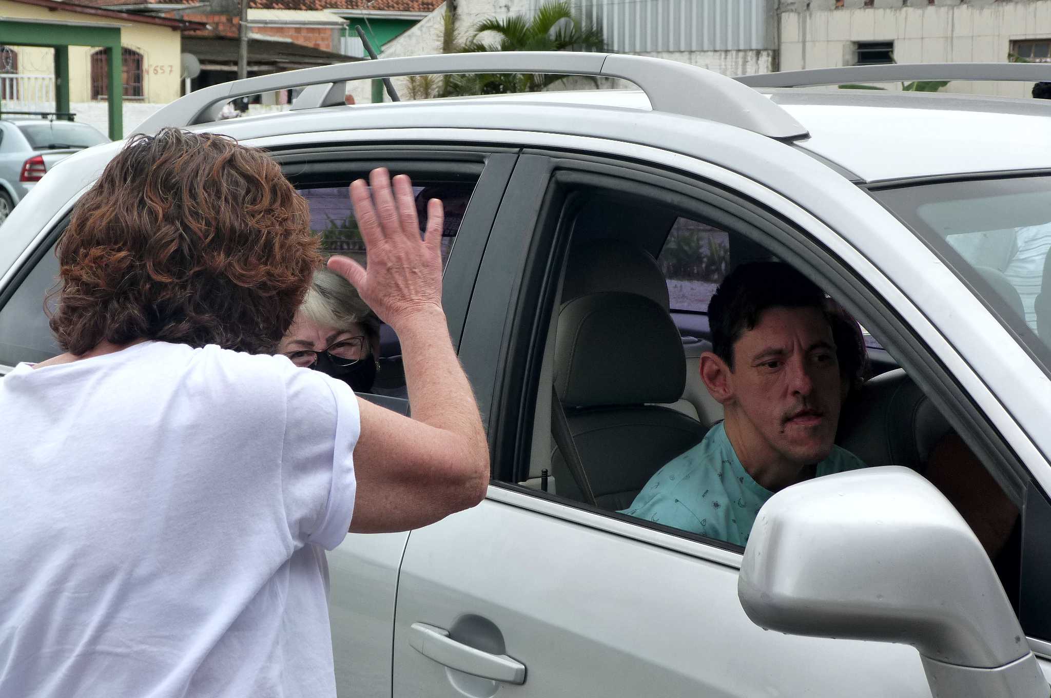 Mulher parada acena para dentro de veículo com vários educandos dentro.