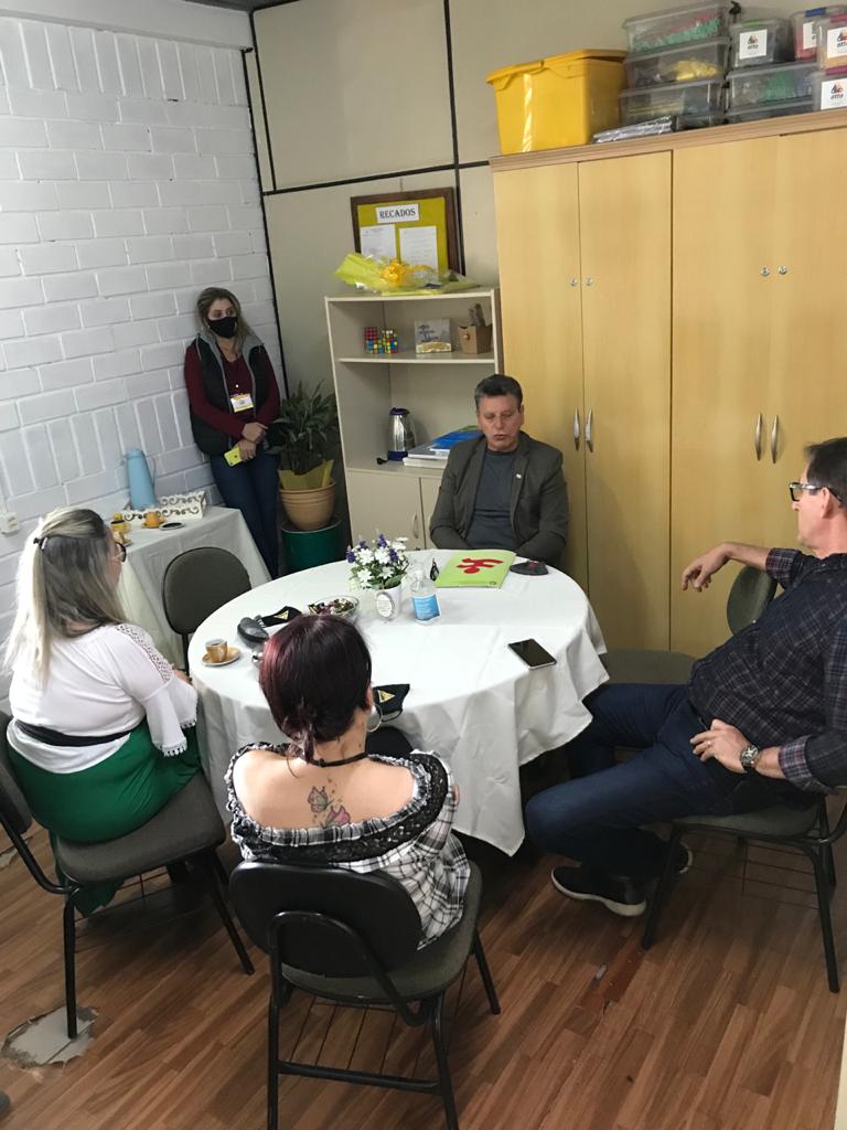 Quatro pessoas sentadas em mesa redonda em ambiente interno. 