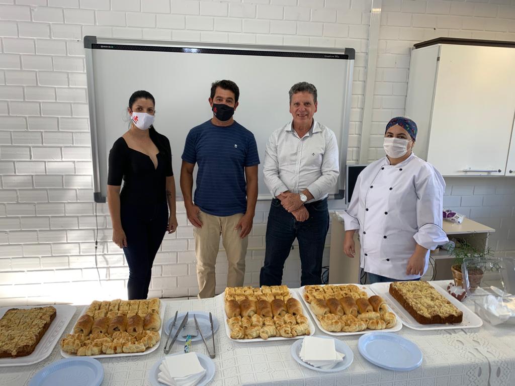 Quatro pessoas em pé posam para foto diante de mesa com toalha branca e pratos com salgados