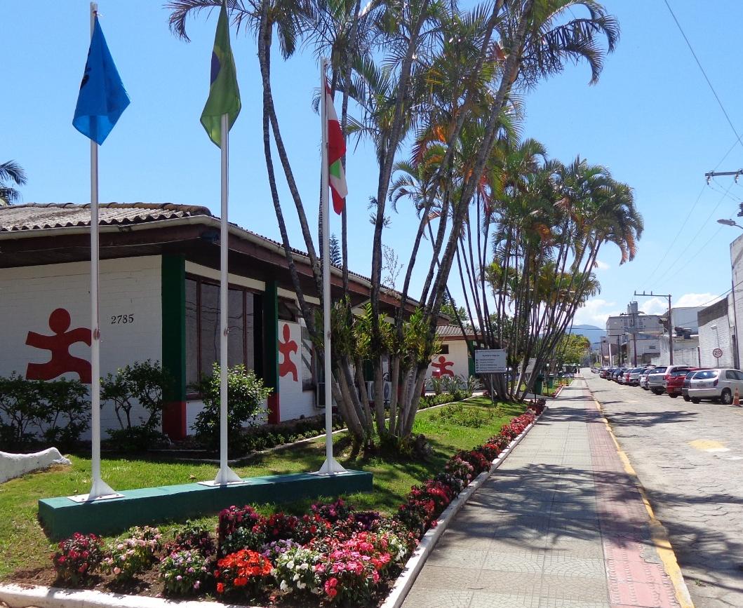 imagem de prédio do campus, dia ensolarado, 3 maços com bandeiras, canteiros com grama e flores