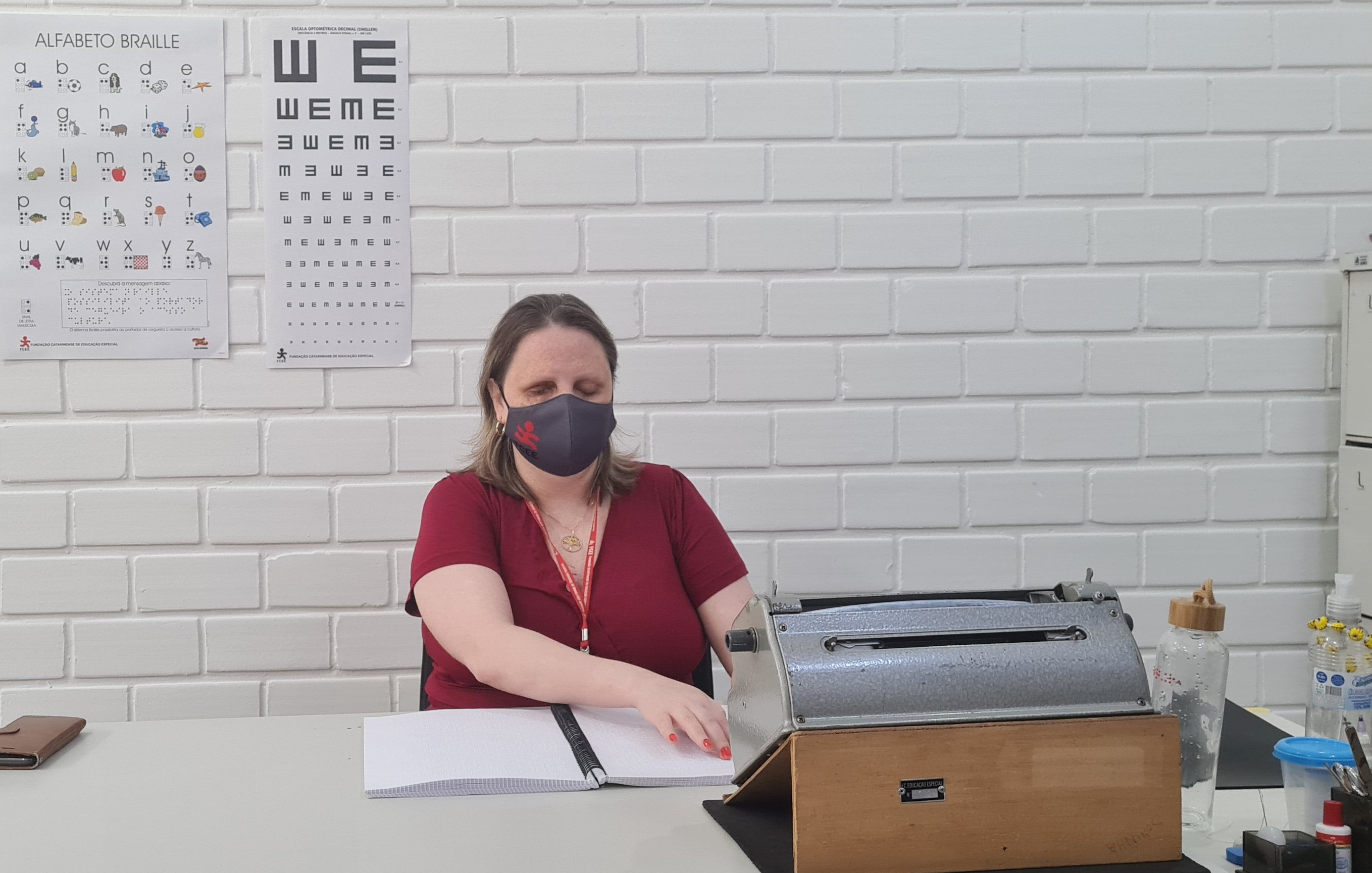 Mulher em ambiente interno, sentada tateando um livro em braile sobre uma mesa