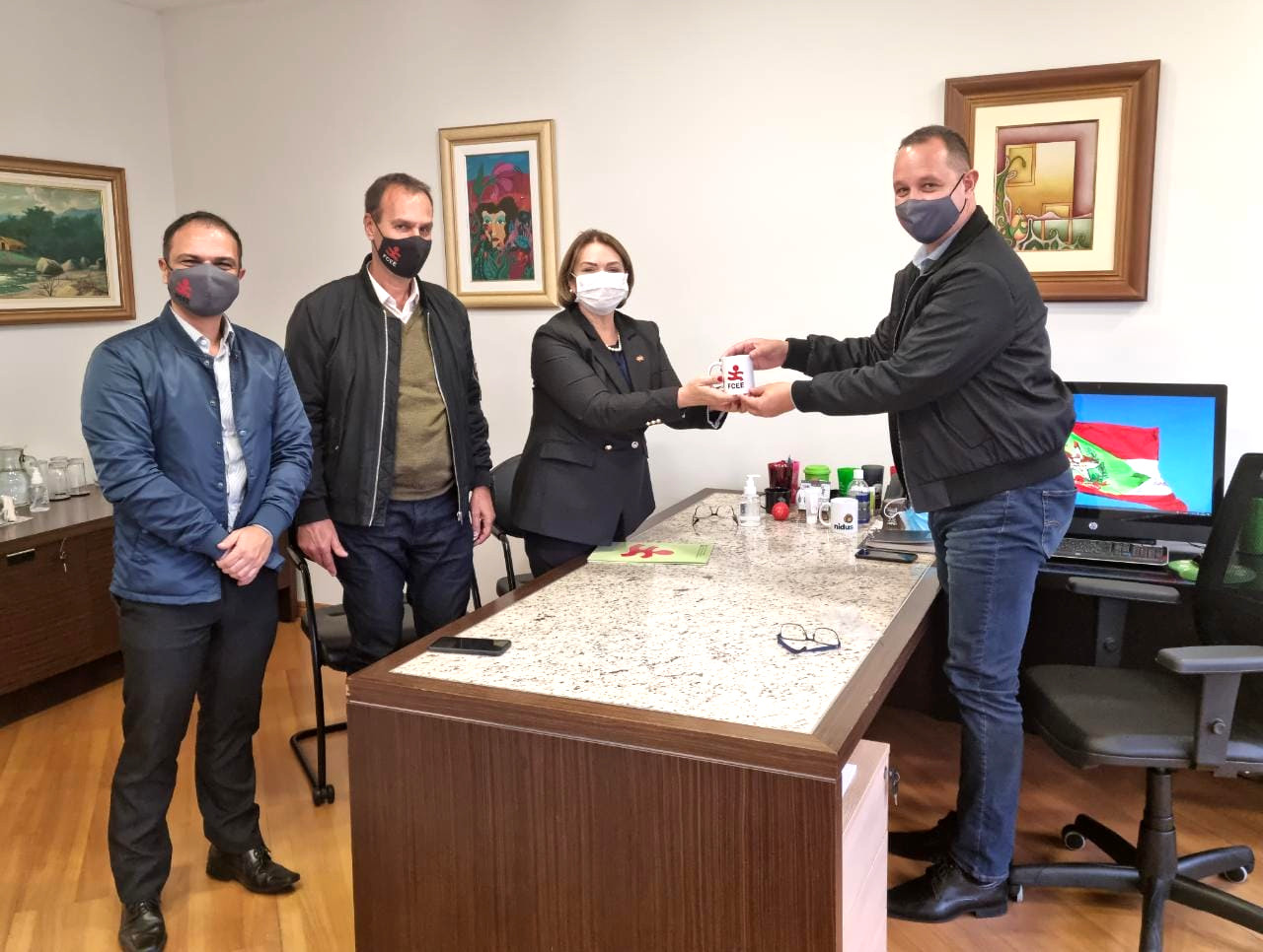 Ambiente interno, escritório, Quatro pessoas em pé, posam para foto, segurando caneca branca