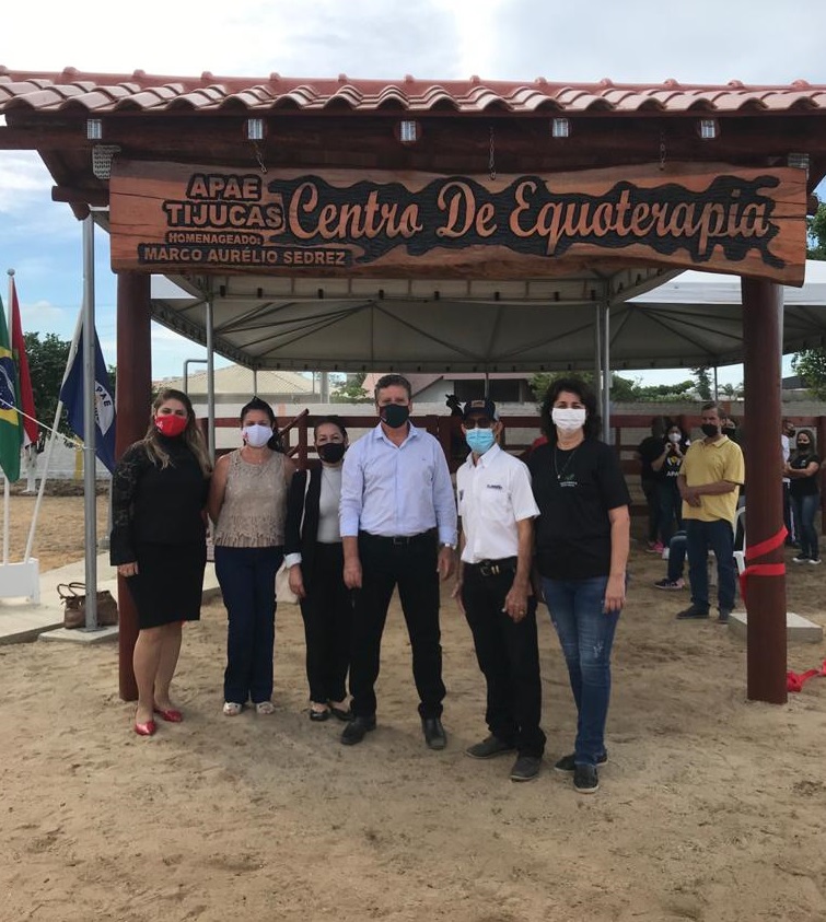 Seis pessoas em pé posam para foto, ambiente aberto, chão de terra clara, pórtico escrito Centro de Equoterapia.  