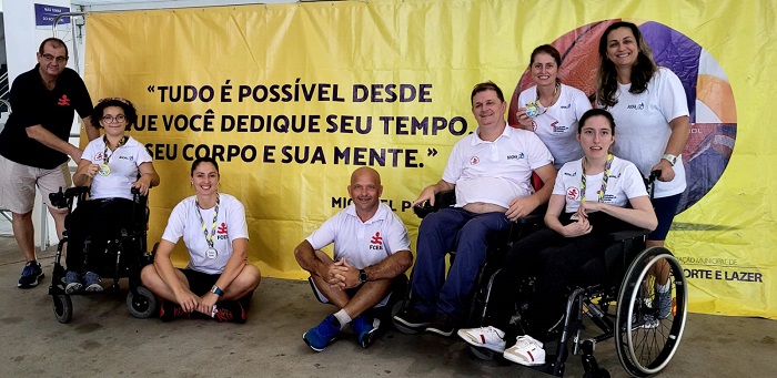 Oito pessoas posam para foto. Duas pessoas com deficiência física, usuárias de cadeiras de rodas, e todos usando camisetas brancas com a logo da Fundação Catarinense de Educação Especial