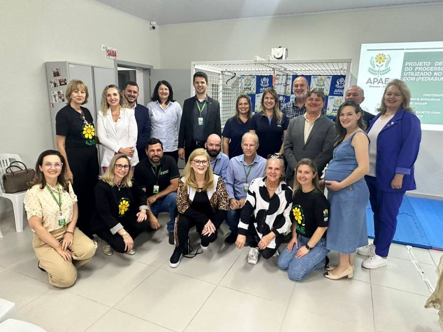 Dez pessoas posam para foto em ambiente interno, ao fundo espécie de esteira de caminhar com faixas. 