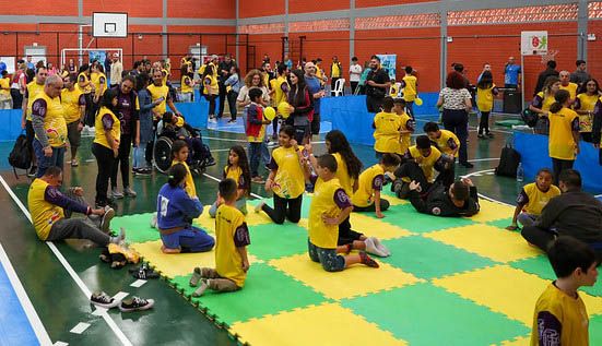  crianças com camisetas amarelas em ginásio, tatames verde e amarelo